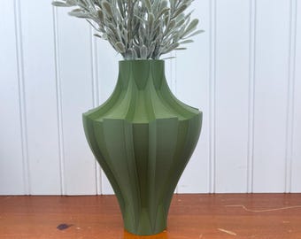 May include: A green ceramic vase with a ribbed design. The vase is tall and narrow, with a rounded base and a flared top. It is filled with a bouquet of dried greenery.