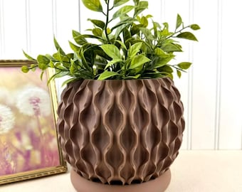 May include: A brown, textured plant pot with a matching saucer, filled with green leafy plants. The pot features a repeating wave pattern. The plant pot is a stylish home decor item.