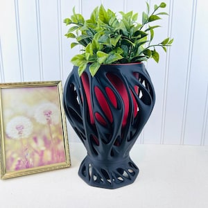 May include: Black planter with a red interior and a unique, organic, branch-like design. A small green plant is in the planter.