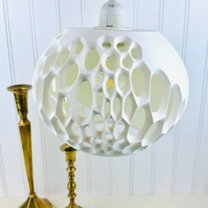May include: White pendant light fixture with a geometric, honeycomb-like design. The light fixture is made of a white material and has a round shape.