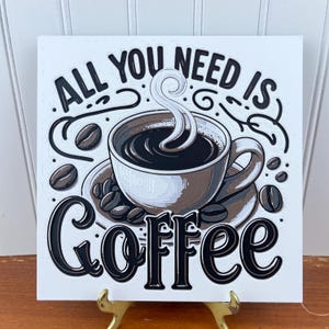 Könnte beinhalten: Ein weißes quadratisches Schild mit schwarzer Aufschrift, die "Alles was du brauchst ist Kaffee" lautet. Eine Comic-Illustration einer dampfenden Tasse Kaffee mit einem Wirbel aus Dampf befindet sich in der Mitte des Schildes.