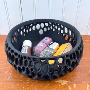 May include: A black, 3D printed, honeycomb-shaped bowl with four bottles of nail polish inside. The bowl has a textured, organic design.
