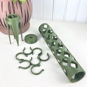 Peut inclure: Divers accessoires d'arrangement floral vert olive. L'image présente une cage cylindrique à motif losange, un piquet à trois pieds, un petit disque et plusieurs clips en forme de U. Ces éléments sont pour les compositions florales.