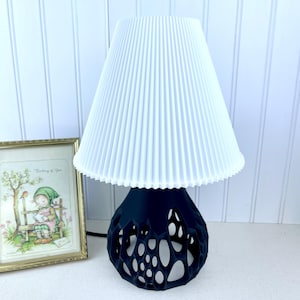 May include: A black table lamp with a white pleated lampshade. The lamp base has a unique, openwork design.