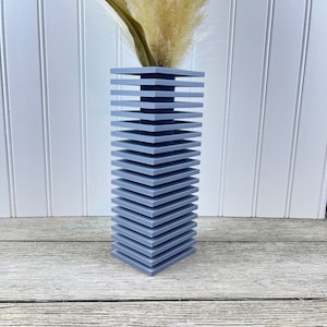 May include: A gray ceramic vase with a stacked design. The vase is made of multiple square pieces stacked on top of each other. The vase is empty and ready to hold flowers.