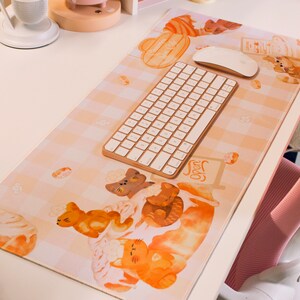 May include: A white desk mat with a checkered pattern and cute cartoon illustrations of cats and pastries. The mat features a wireless keyboard and mouse, and the text "Open" is visible on a sign.