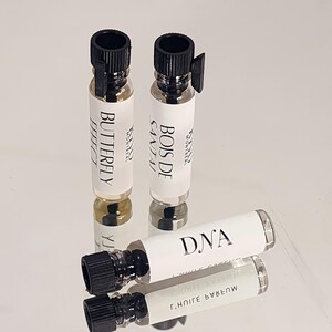 May include: Three small glass bottles with black caps and labels. The labels read "Bois de Santal", "Butterfly Effect", and "DNA".