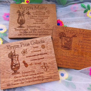 May include: Three wooden coasters with engraved cocktail recipes: Virgin Mary, Virgin Mojito, and Virgin Pina Colada. Each coaster features a detailed illustration of the drink and its ingredients, with text in a decorative font.