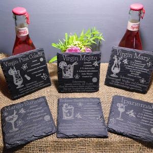May include: A collection of six dark gray slate coasters with engraved cocktail recipes, including "Virgin Pina Colada," "Virgin Mojito," and "Virgin Mary." Two bottles of red spritz are in the background.