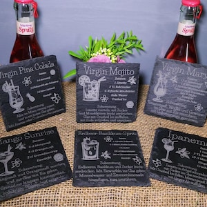May include: Six black slate coasters with engraved cocktail recipes, including Virgin Pi&ntilde;a Colada, Virgin Mojito, Virgin Mary, Mango Sunrise, Erdbeer Basilikum-Spritz, and Ipanema. The coasters are arranged on a burlap surface, with two bottles of red liquid in the background.