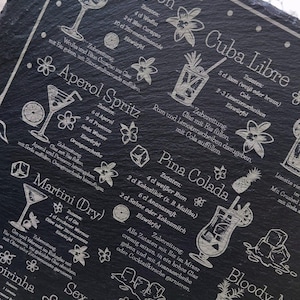 May include: A black slate serving board etched with cocktail recipes, including Blue Lagoon, Cuba Libre, and Martini (Dry). The board features detailed illustrations of each drink and their ingredients, with white text. A decorative and functional item.