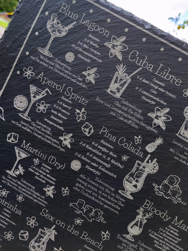 May include: A black slate serving board etched with cocktail recipes, including Blue Lagoon, Cuba Libre, and Martini (Dry). The board features detailed illustrations of each drink and their ingredients, with white text. A decorative and functional item.