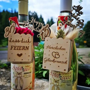 May include: Two bottles of Apfelrecco rose wine, each adorned with wooden decorations. One features a "30" and "Happy Birthday" topper, the other a "Herzlichen Glückwunsch" sign. The labels display an owl illustration.