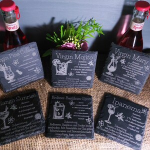 May include: A collection of six slate coasters with cocktail recipes engraved in white. The coasters include recipes for Virgin Pina Colada, Virgin Mojito, Virgin Mary, Mango Sunrise, Erdbeer-Basilikum-Sprit, and Ipanema. Two bottles of Spritz are in the background.