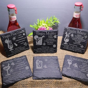 May include: A collection of six dark gray slate coasters with engraved cocktail recipes, including "Virgin Pina Colada," "Virgin Mojito," and "Virgin Mary." Two bottles of red spritz are in the background.