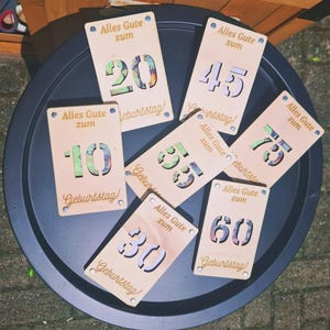 May include: Wooden birthday cards with laser-cut numbers 10, 20, 30, 45, 55, 60, and 75. Each card has the German text "Alles Gute zum Geburtstag!" and is decorated with blue dots.