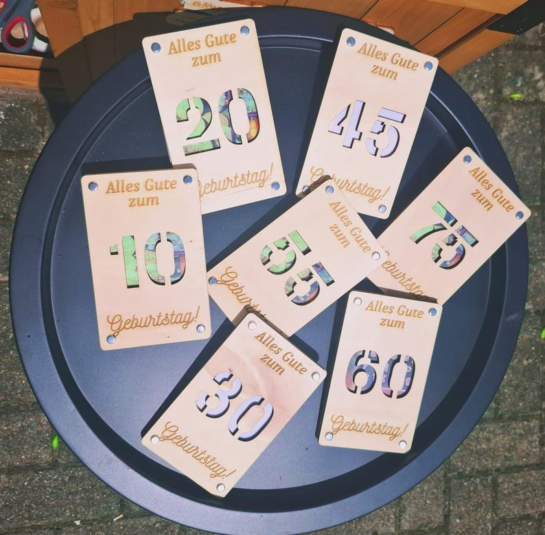 May include: Wooden birthday cards with laser-cut numbers 10, 20, 30, 45, 55, 60, and 75. Each card has the German text "Alles Gute zum Geburtstag!" and is decorated with blue dots.