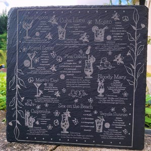 May include: A dark gray slate serving board etched with cocktail recipes, including Blue Lagoon, Mojito, and Pina Colada. The board features detailed illustrations of each drink and their ingredients, with floral accents.