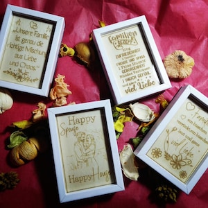 May include: Four framed wooden plaques with white borders, each featuring engraved text and designs. The plaques rest on a red surface with dried flowers and leaves. The text includes phrases like "Happy Spouse" and "Family".