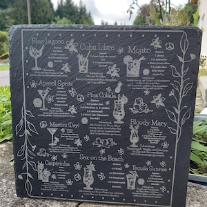 May include: A dark gray slate serving board etched with cocktail recipes. The board features detailed illustrations and instructions for drinks like Mojito, Pina Colada, and Tequila Sunrise, with decorative floral accents.