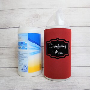 May include: A white container of disinfecting wipes and a red bottle with a black label that reads "Disinfecting Wipes". The label is in a decorative frame. The background is a light wood grain.