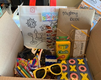May include: A cardboard box filled with various items, including a colouring book, a mystery book, a pack of chalk, a pair of sunglasses, a pop-it fidget toy, a bag of sweets, a pair of socks, and a noughts and crosses game.