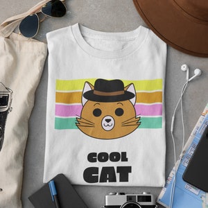 May include: White t-shirt with a cartoon cat wearing a hat and sunglasses. The cat is on a striped background with the text "COOL CAT" below it.