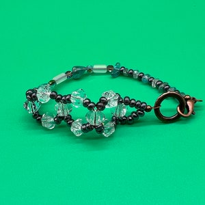 May include: A beaded bracelet with clear faceted beads, dark gray beads, and blue and green beads. The bracelet has a copper clasp.