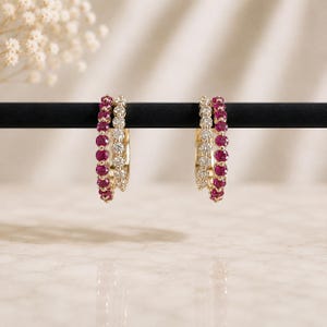 Könnte beinhalten: Ein Paar Creolen mit zweireihigem Design. Jeder Ohrring besteht aus einer Reihe runder, leuchtend pinker Rubine und einer Reihe klarer, funkelnder weißer Diamanten, die in ein poliertes Goldmetallband gefasst sind und einen Lagen-Look erzeugen.
