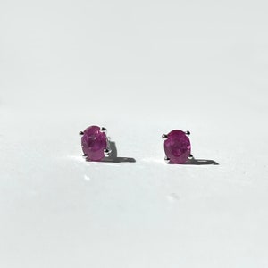 May include: A pair of silver stud earrings with oval-shaped pink gemstones.
