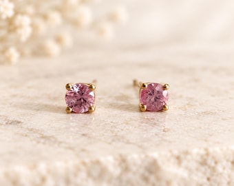Pode incluir: Um par de brincos de tarracha com pedras preciosas cor-de-rosa redondas e facetadas engastadas em metal dourado. Cada pedra é fixada por quatro pequenas garras, criando um design clássico que destaca a cor rosa vibrante das pedras.