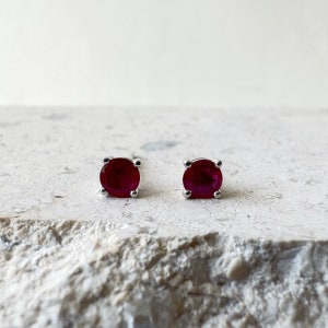 May include: A pair of silver stud earrings with round red ruby gemstones.