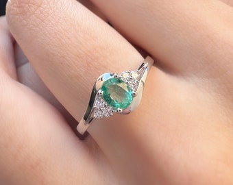 May include: A silver ring with a green oval emerald gemstone and smaller clear gemstones set in a curved band.