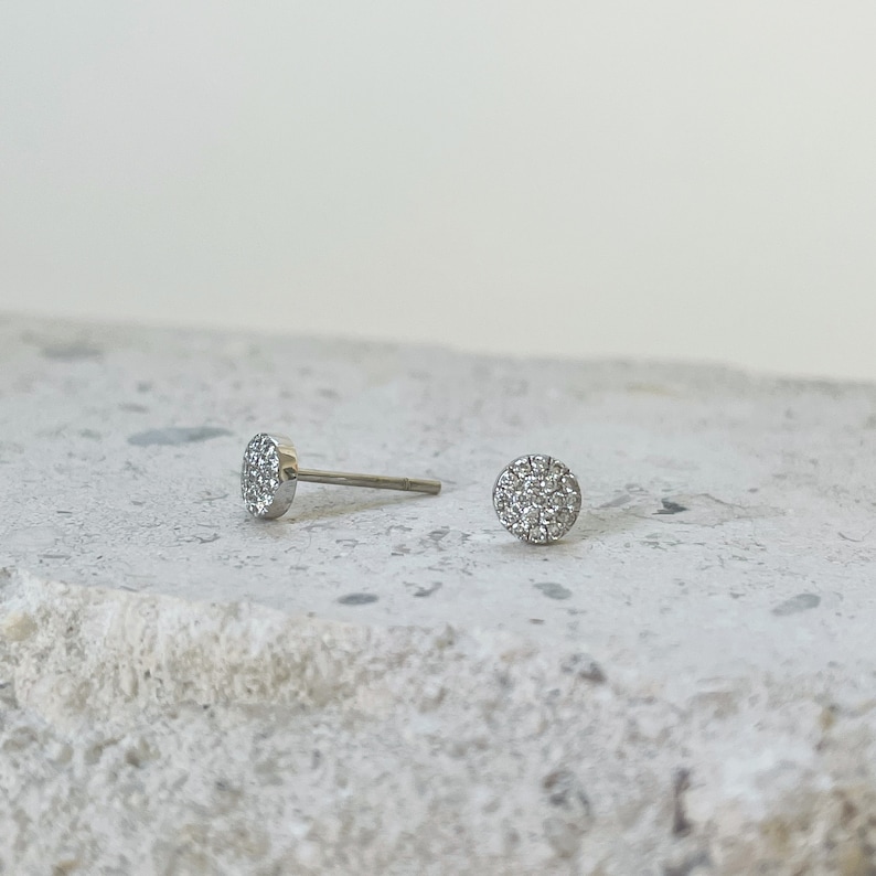 Puede incluir: Un par de pendientes de bot&oacute;n de plata con un dise&ntilde;o redondo de diamantes pav&eacute;.