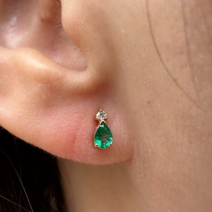 May include: A pair of gold earrings with a pear-shaped emerald gemstone and a small round diamond accent.