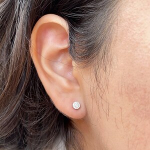 Puede incluir: Primer plano de una oreja con un peque&ntilde;o pendiente de diamante redondo. El pendiente est&aacute; engastado en un engaste de plata u oro blanco.