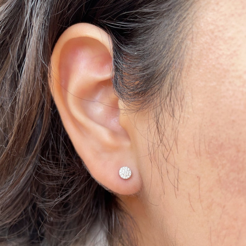 Puede incluir: Primer plano de una oreja con un peque&ntilde;o pendiente de diamante redondo. El pendiente est&aacute; engastado en un engaste de plata u oro blanco.