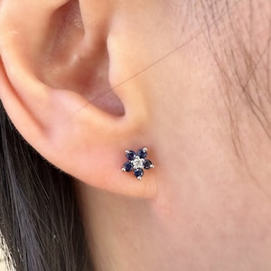 Puede incluir: Un par de pendientes de plata en forma de flor con piedras preciosas azules y blancas.