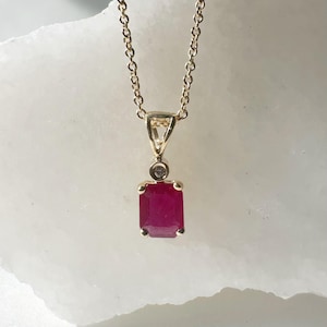 May include: A gold chain necklace with a pendant featuring a red emerald-cut ruby and a small diamond accent.