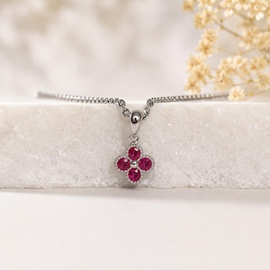 May include: A silver-toned necklace featuring a pendant shaped like a four-leaf clover. The pendant is set with four round, vibrant pink gemstones arranged in a floral pattern, suspended from a delicate silver-toned chain with a polished finish.