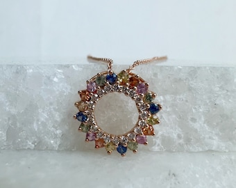 May include: A rose gold necklace featuring a circular pendant adorned with a vibrant array of colorful gemstones. The pendant's design includes a central open circle surrounded by a halo of multi-colored stones, creating a radiant and eye-catching piece of jewelry.