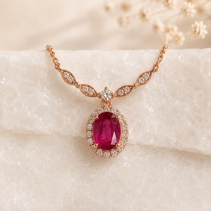 May include: A rose gold necklace featuring an oval-cut deep red ruby pendant surrounded by a halo of small white diamonds. The chain includes marquise-shaped links, each set with tiny white diamonds, connecting to the central ruby pendant.