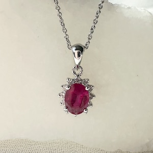 May include: A silver chain necklace with a pendant featuring a large oval ruby surrounded by a halo of smaller diamonds.