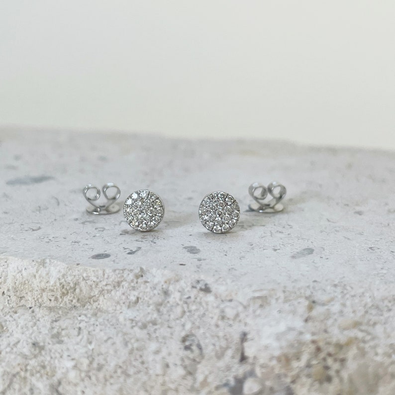 Puede incluir: Un par de pendientes de bot&oacute;n de plata con un dise&ntilde;o redondo de diamantes pav&eacute;.