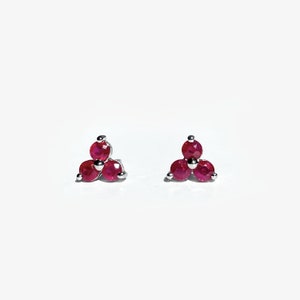 May include: A pair of silver stud earrings with three red ruby stones in a triangular shape.