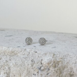 Puede incluir: Un par de pendientes de bot&oacute;n de plata con un dise&ntilde;o redondo de diamantes pav&eacute;.