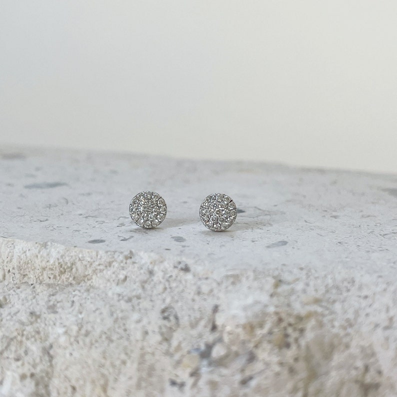 Puede incluir: Un par de pendientes de bot&oacute;n de plata con un dise&ntilde;o redondo de diamantes pav&eacute;.