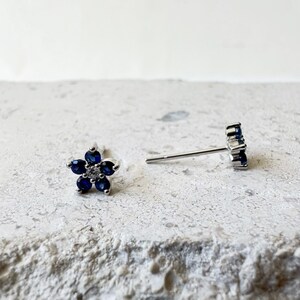 Puede incluir: Un par de pendientes de bot&oacute;n de plata con piedras azules en forma de flor. Los pendientes est&aacute;n sobre una superficie blanca.