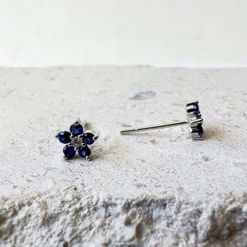 Puede incluir: Un par de pendientes de bot&oacute;n de plata con piedras azules en forma de flor. Los pendientes est&aacute;n sobre una superficie blanca.
