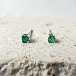 Puede incluir: Un par de pendientes de plata con pequeñas piedras de esmeralda redondas y verdes.